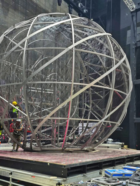 Photo of large steel orb feature upon a stage during installation