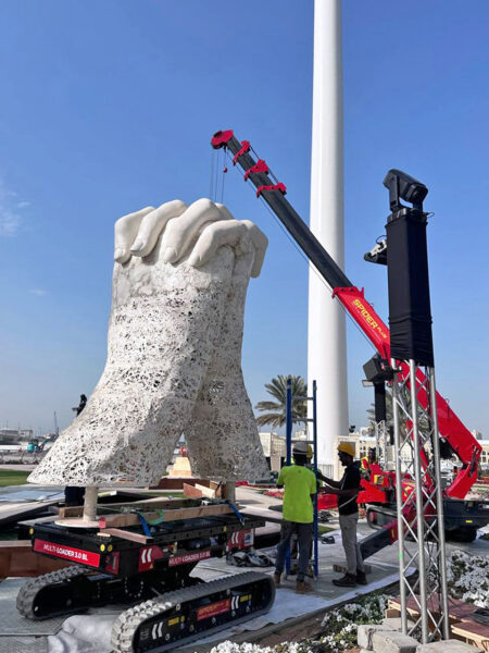 Image of large-scale hand artwork being lifted and installed by crane