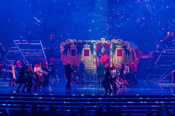 Image of on stage performance, performers in front of a decorative caravan stage set