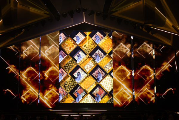 Image of stage performance with diamond shaped grid wall with live performers