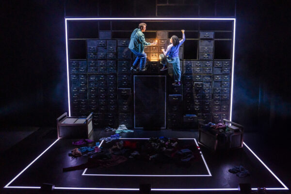 Man and woman theatre performers climbing a structure that resembles a filing cabinet