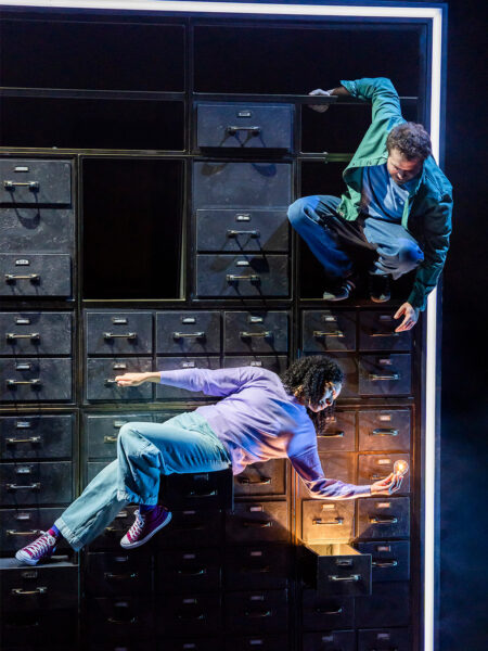 Photo of man and woman theatre performers positioned on the face of large-scale filing-cabinet-like structure