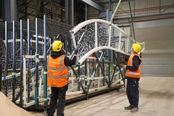 Photo of two people supporting a steel frame being lifted in the air for loading